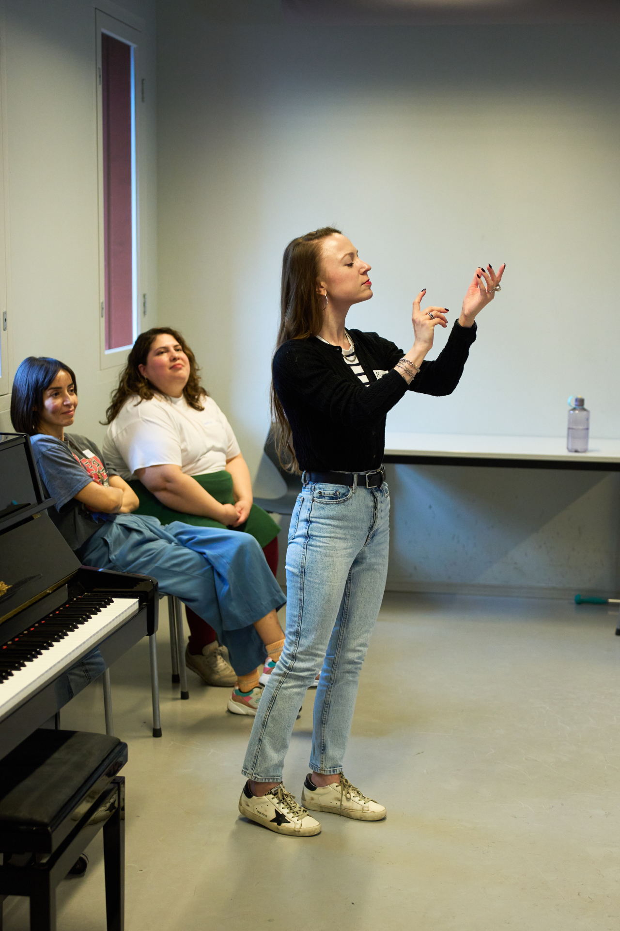 Verónica demonstrating a gesture exercise while two participants watch near a piano